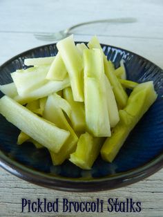 pickled broccoli stalks in a blue bowl on a wooden table with the words pickled broccoli stalks