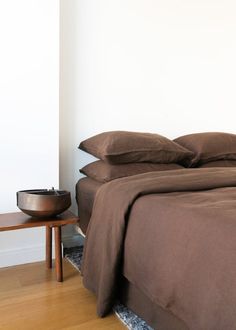 a bed with brown sheets and pillows in a white room next to a wooden table