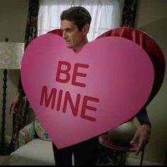 a man holding a pink heart shaped sign with the words be mine written on it