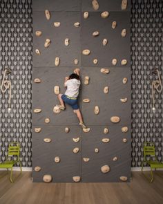 a man climbing up the side of a rock wall in a room with wood floors