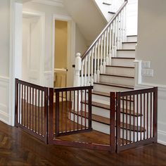 an open gate in the middle of a wooden floor next to a stair case and white walls