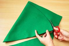 someone cutting fabric with scissors on top of a green piece of cloth that has been cut into smaller pieces