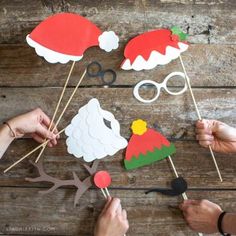 some people are making santa hats out of paper and wood sticks on a wooden table