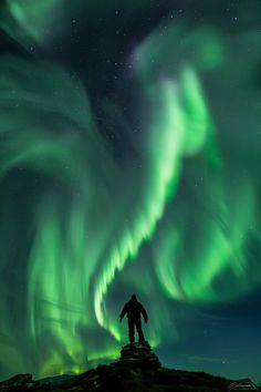 a man standing on top of a hill under the aurora lights