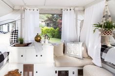 the inside of a camper with white curtains and plaid pillows