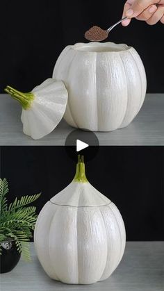 a person holding a spoon in front of two white pumpkins with leaves on them