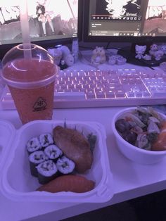 a plastic container filled with lots of food next to a cup of juice and computer keyboard