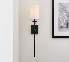 a wall mounted lamp with a white shade on it's side next to a framed photograph