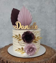 a white cake with purple flowers and leaves on top is sitting on a tree stump