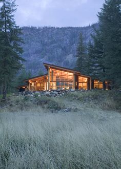 the cabin is lit up at night in the mountains with tall grass and trees around it