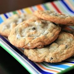 three chocolate chip cookies on a colorful striped plate with a glass of milk in the background