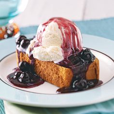 a piece of cake covered in ice cream and blueberry sauce on a white plate