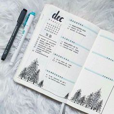 an open planner with trees on it and a pen next to it, sitting on a furry surface