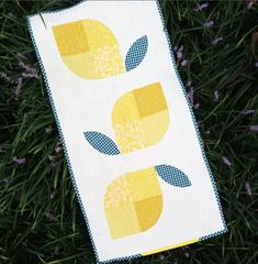 a yellow and white quilt with two lemons on the front, sitting in some grass