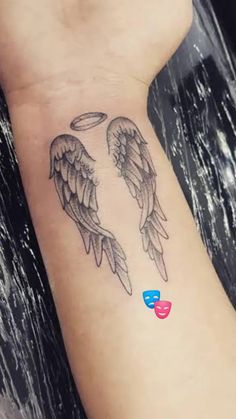 an angel wing tattoo on the wrist with a heart shaped object in front of it