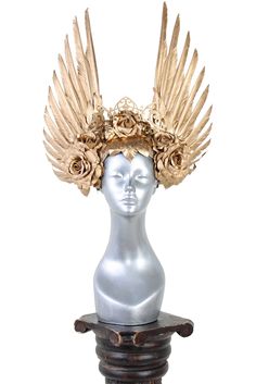 Hand assembled feathered wings arise amongst golden roses, offering its wearer a crown of gilded victory. One-of-a-kind couture wearable art Handcrafted All headgear sales are final. Due to the unique nature of these works of art, coupon codes will not be accepted. Measurements6" internal head width, 13" height, 14" width Gold Fantasy Costume Hats And Headpieces, Fantasy Gold Headpiece For Costume, Seraphim Headpiece, Warrior Crown, Rose Headdress, Gold Headdress Goddesses, Mythology Costumes, Elaborate Headdress, Feathered Wings