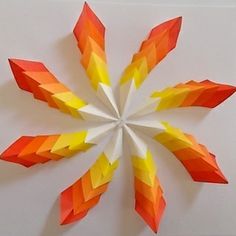 an orange, yellow and red paper flower on a white surface with the center cut out