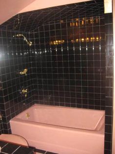 a bathroom with black and gold tiles on the walls, tub and toilet in it