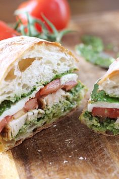 a cut in half sandwich sitting on top of a wooden cutting board next to tomatoes