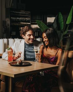 a man and woman sitting at a table with food in front of them, smiling