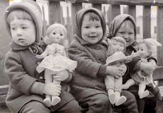 an old black and white photo of four children with dolls in their hands sitting on a bench