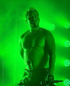 a man with no shirt on standing in front of green lights and holding two chains