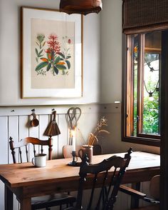 a dining room table with chairs and pictures on the wall above it, in front of a window