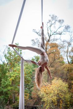 a woman is doing aerial acrobatics on a pole in the middle of a forest