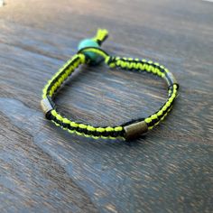 a close up of a bracelet on a wooden table with a green bead and black cord