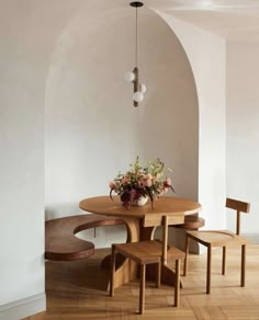 a wooden table with four chairs and a vase on it in front of an arched wall