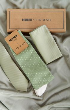 two ties are laying on a bed next to a box that says mumu tie bar