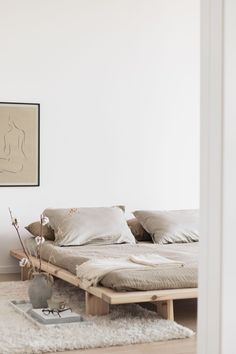 a bed sitting on top of a wooden floor next to a white wall with a painting above it