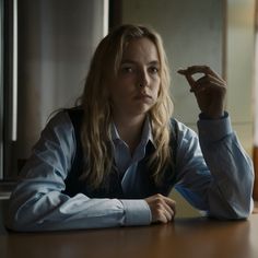 a woman sitting at a table with her hand up to her face and looking off into the distance