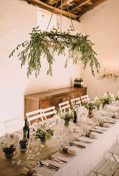 a long table with white chairs and greenery hanging from the ceiling