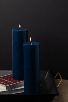 two blue candles sitting on top of a tray next to a book and candle holder