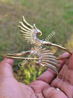 a person is holding a gold brooch with wings and jewels on it's back