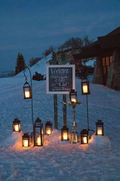 a group of lit candles sitting in the snow next to a sign that says welcome