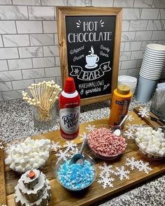 hot chocolate, marshmallows, and candy on a wooden tray with a sign in the background