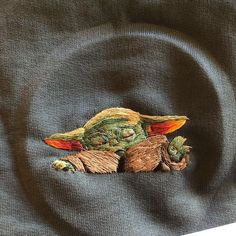 an embroidered image of a baby yoda laying on top of a black fabric background