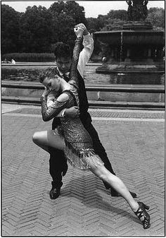 a man and woman are dancing together in the middle of a bricked area with fountain behind them