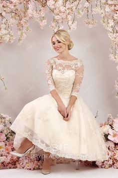 a woman in a white dress sitting on a bench with pink flowers behind her and posing for the camera