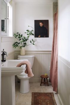 a white toilet sitting next to a sink in a bathroom under a painting on the wall