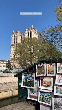 a bunch of pictures are hanging on a wall by the river in front of an old building