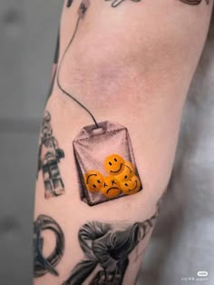 an arm with some tattoos on it and two oranges in a bag attached to the arm