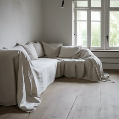 a living room with white walls and wooden flooring that has a couch covered in a blanket