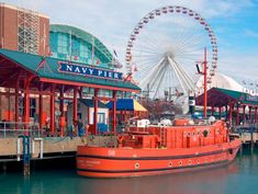 a large red boat sitting in front of a pier with a ferris wheel behind it