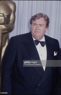 an older man in a tuxedo and bow tie standing next to a statue