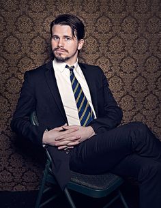 a man in a suit and tie sitting on a chair with his arms folded up