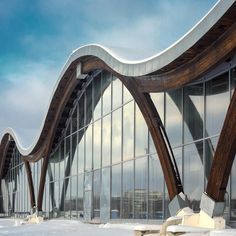 an artistic building with curved wooden and glass windows in the snow covered ground, against a blue cloudy sky