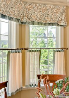 a dining room table with place settings in front of the window and curtains on the windowsill